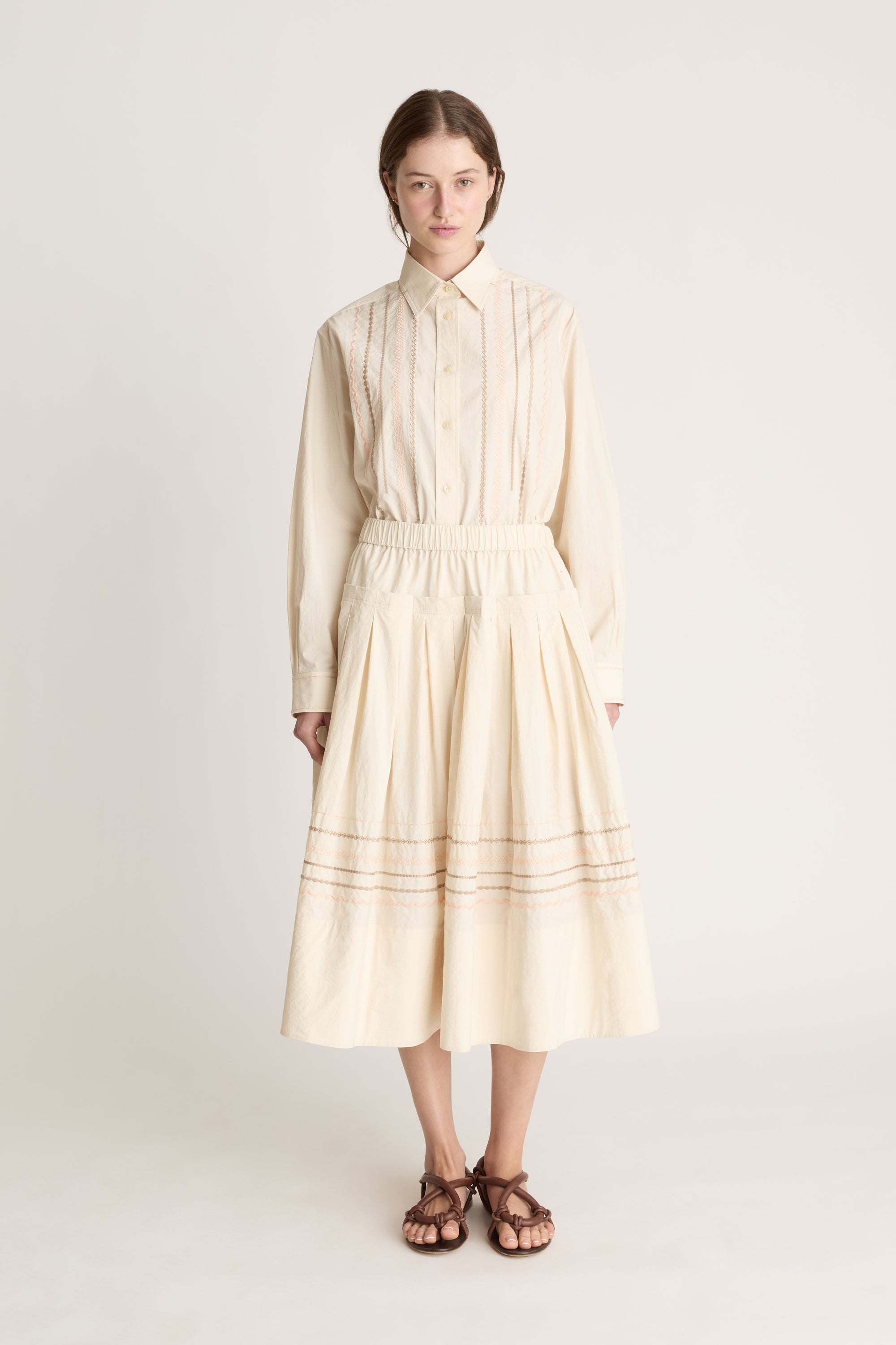 A woman wearing a beige shirt with a beige skirt that has embroidered details.