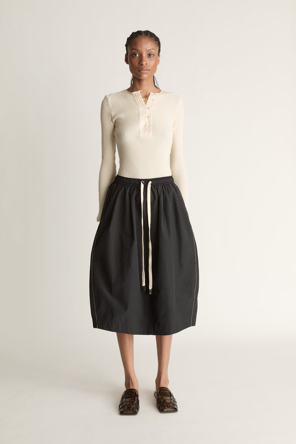 Woman wearing a cream top and black skirt on a white background