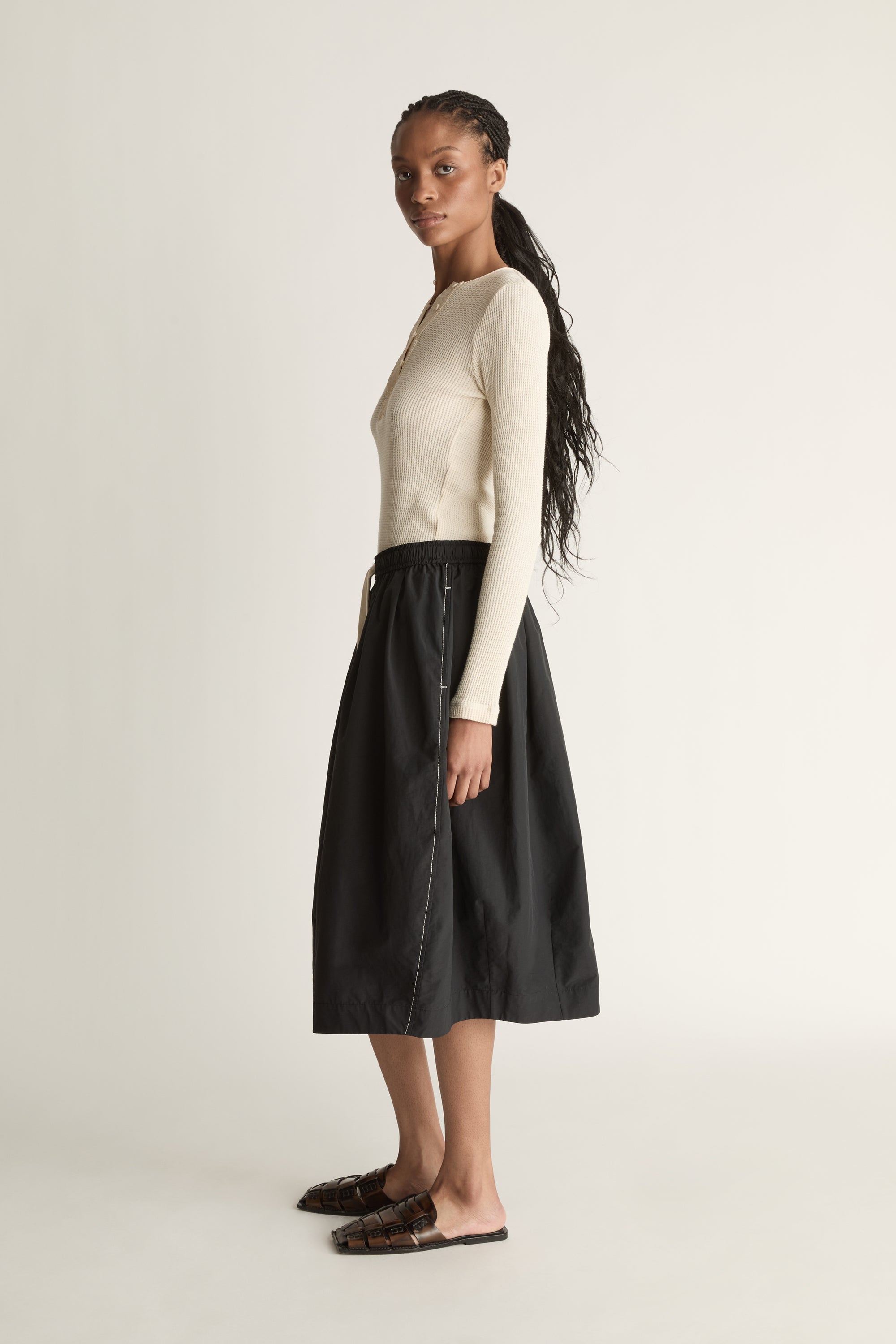 Woman wearing a cream top and black skirt on a white background