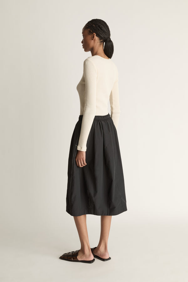 Woman wearing a cream top and black skirt on a white background