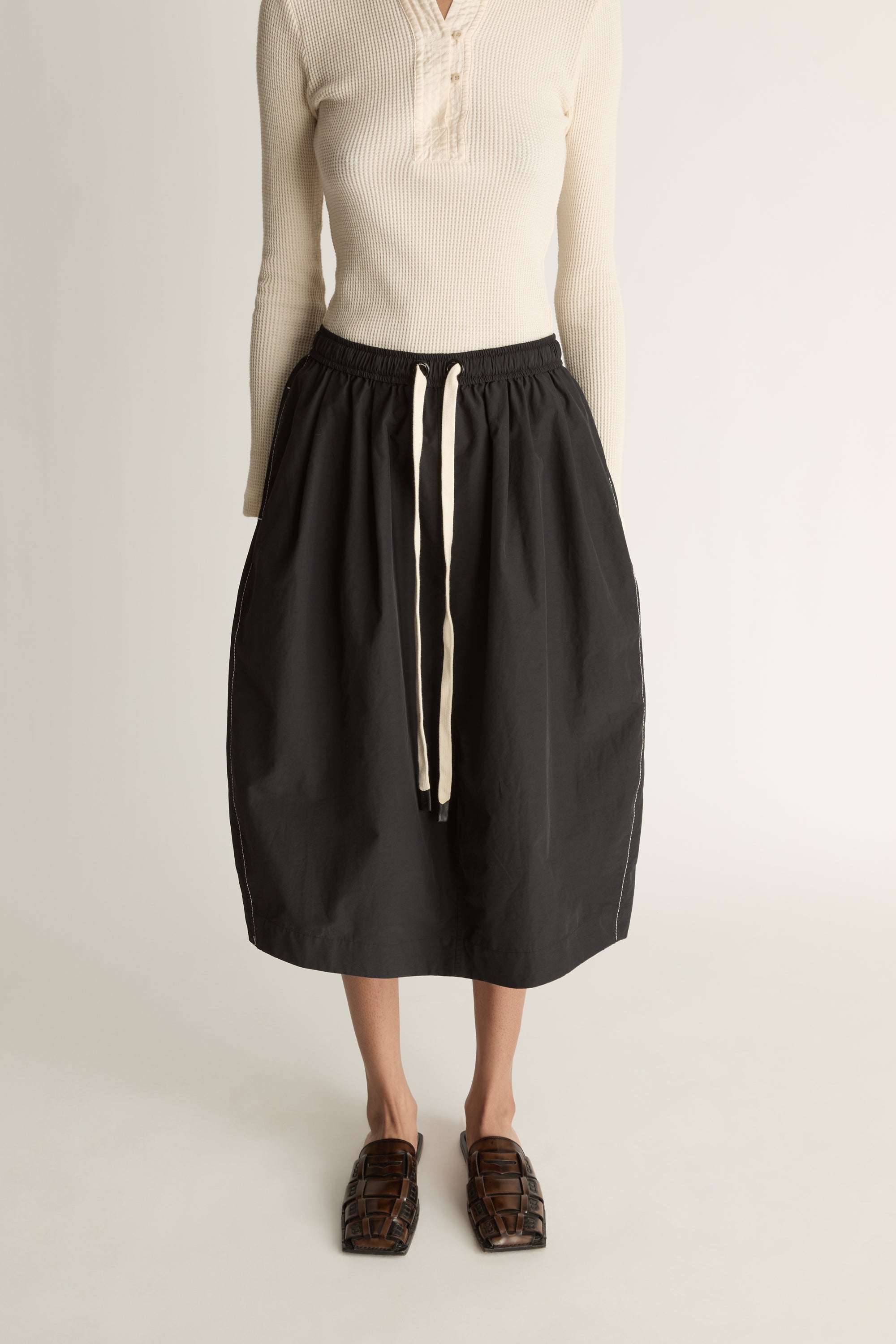 Woman wearing a cream top and black skirt on a white background