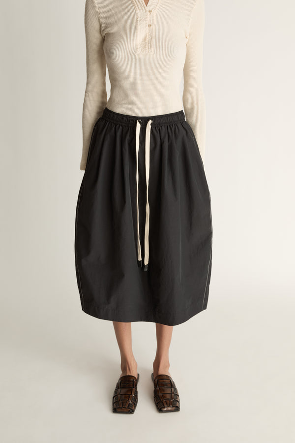 Woman wearing a cream top and black skirt on a white background
