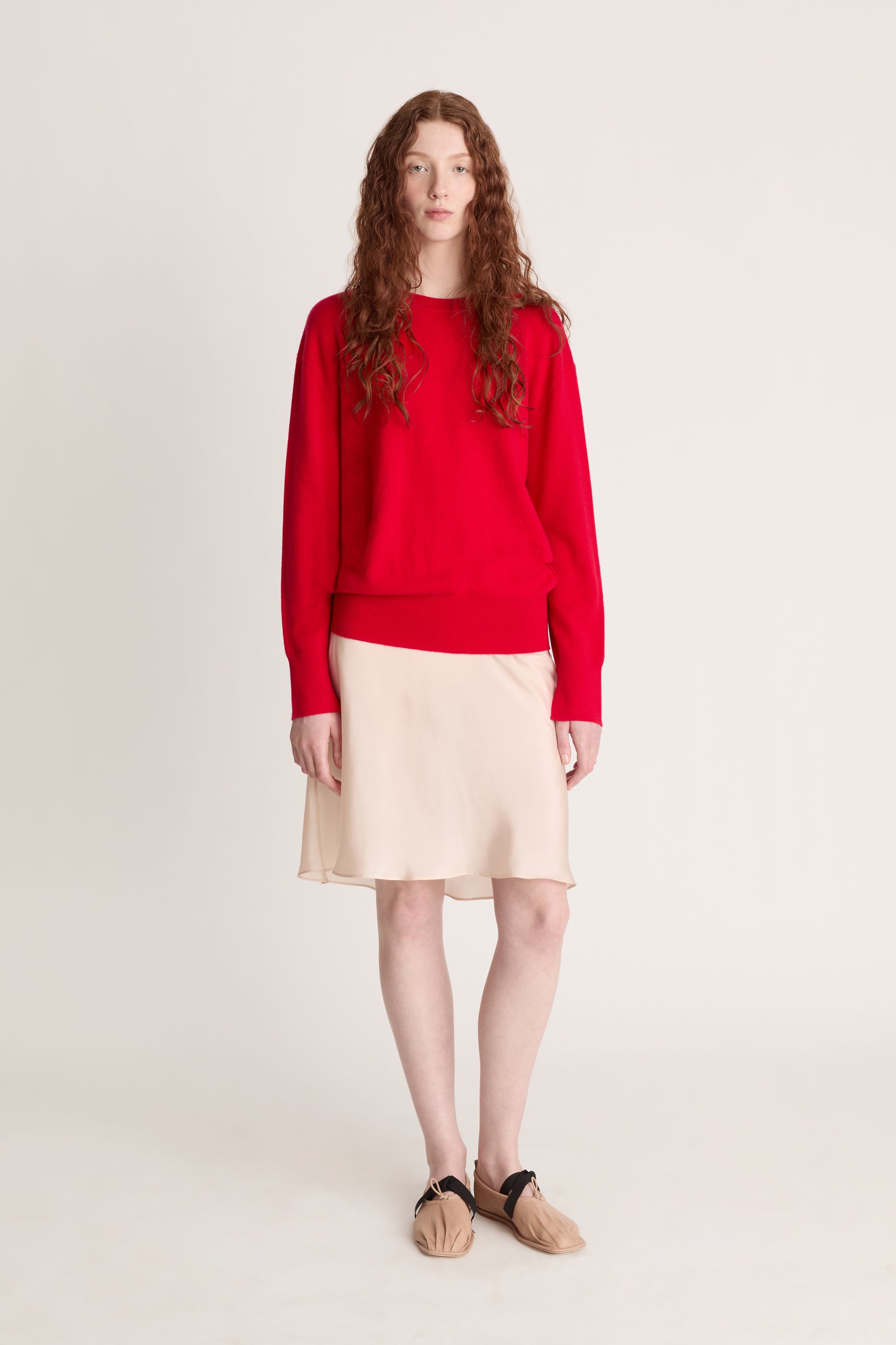 Person wearing a red sweater and beige skirt on a plain background