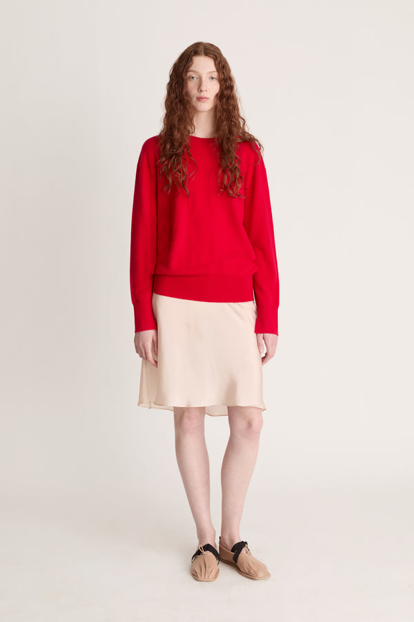 Person wearing a red sweater and beige skirt on a plain background
