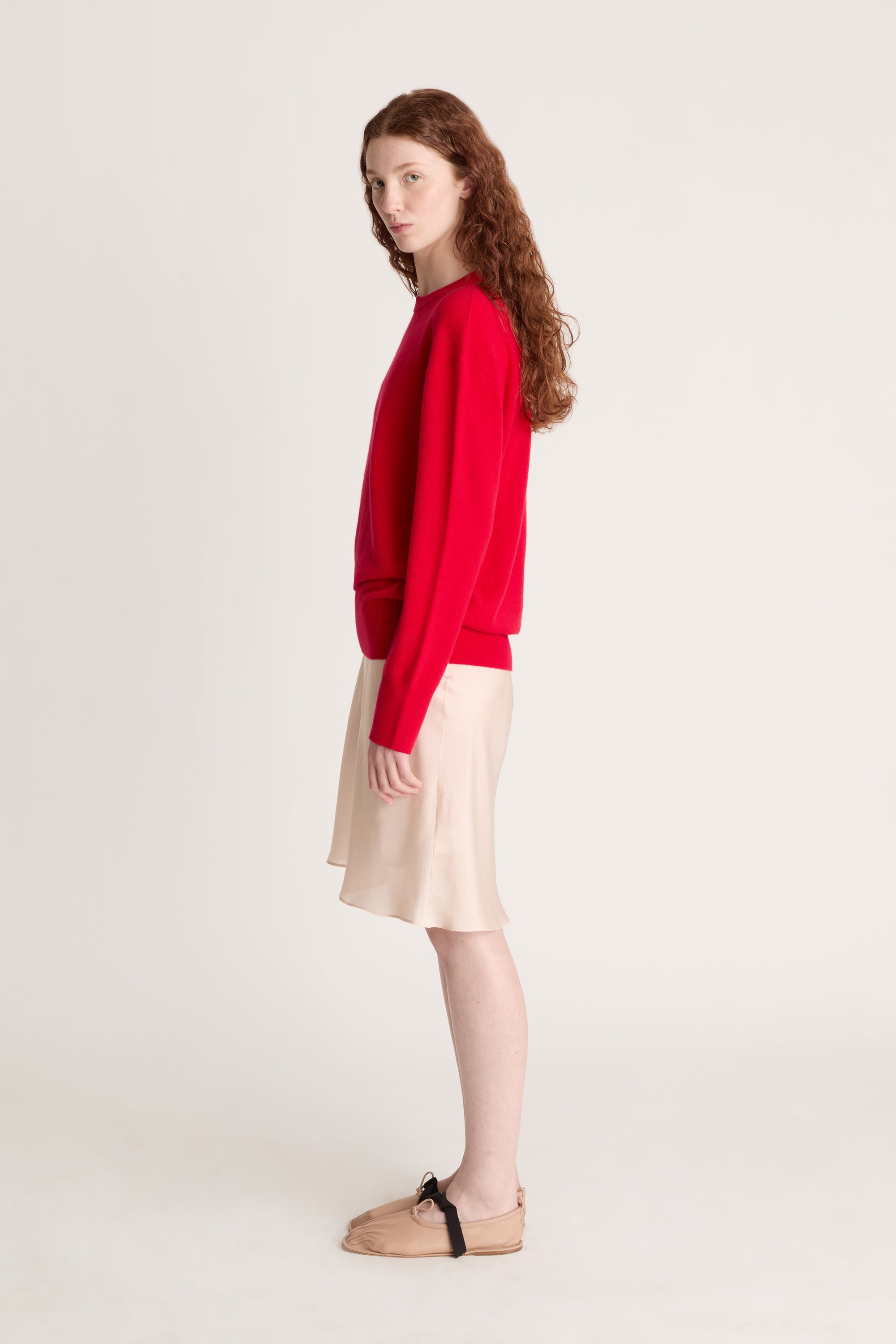 Woman wearing a red sweater and beige skirt on a white background