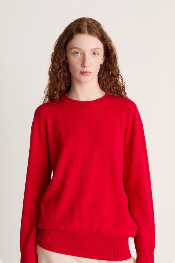 Person wearing a red sweater and beige skirt on a plain background