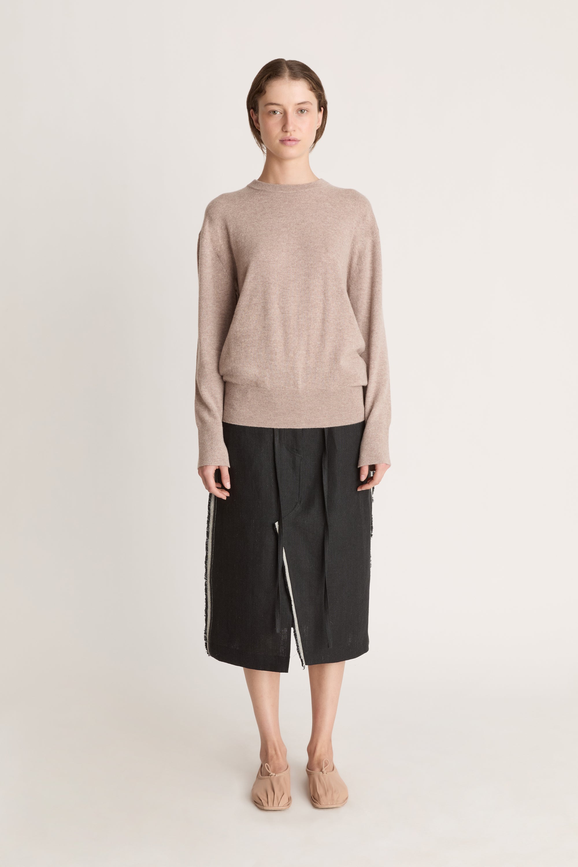 Person wearing a beige sweater and black skirt on a white background