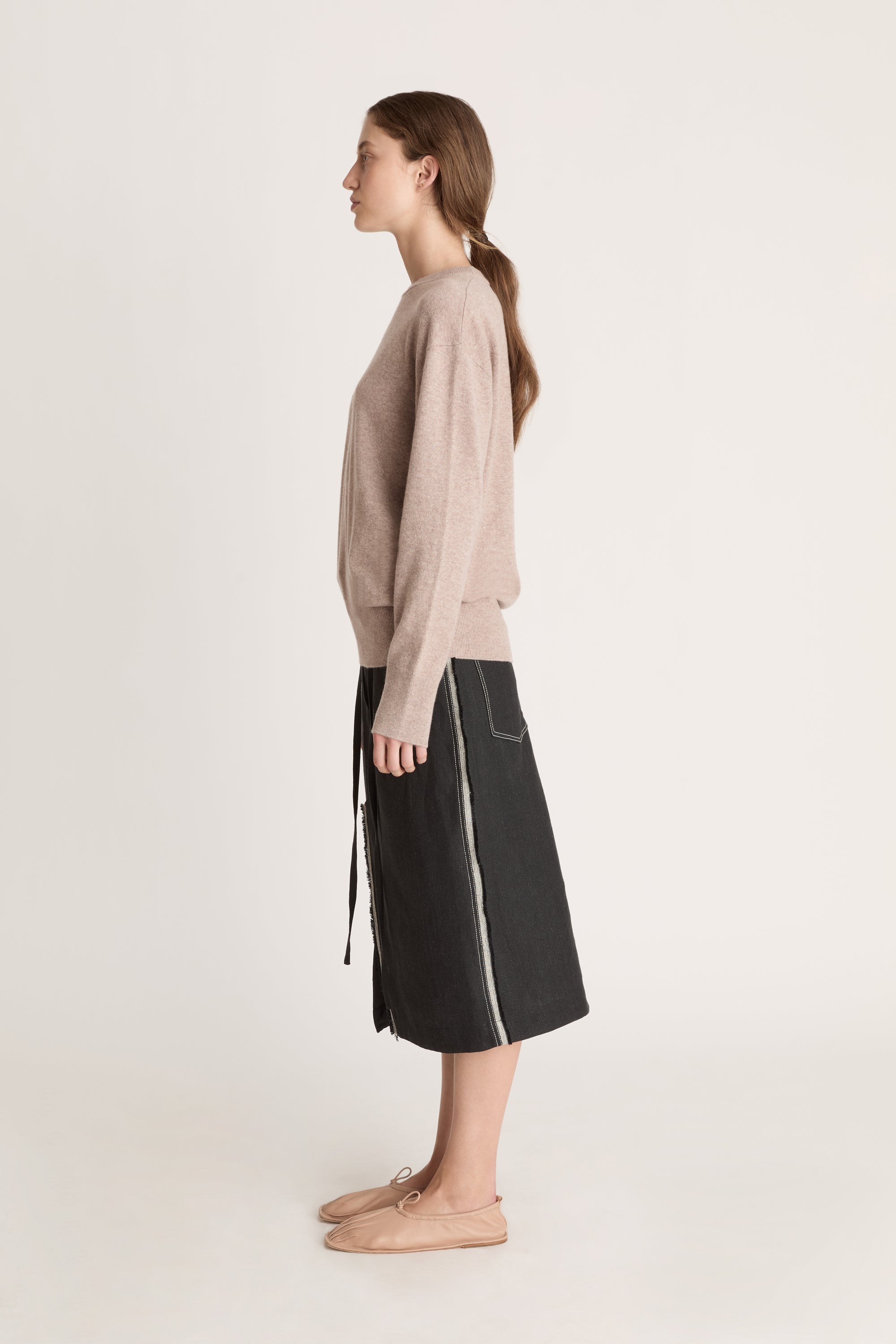 Person wearing a beige sweater and black skirt on a white background