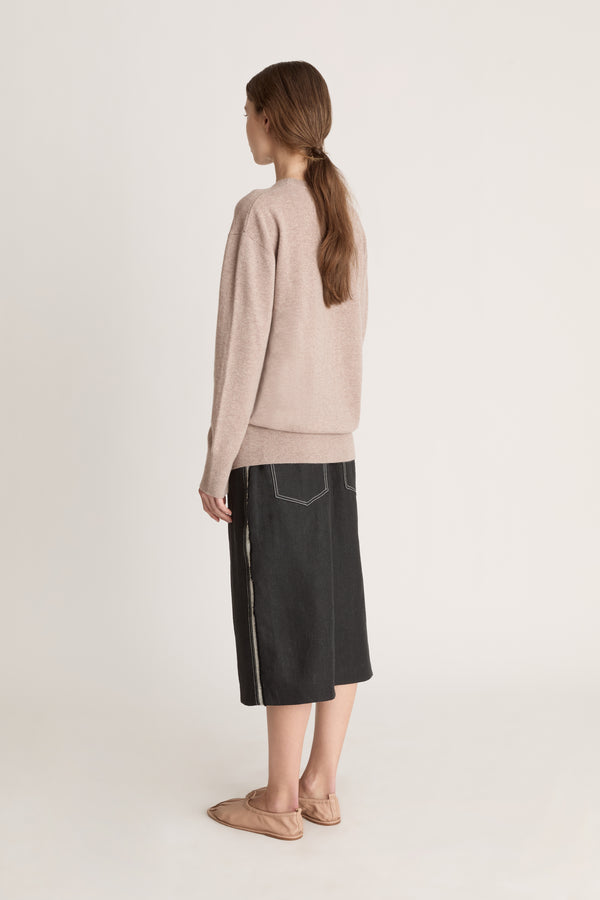 Person wearing a beige sweater and black skirt on a white background