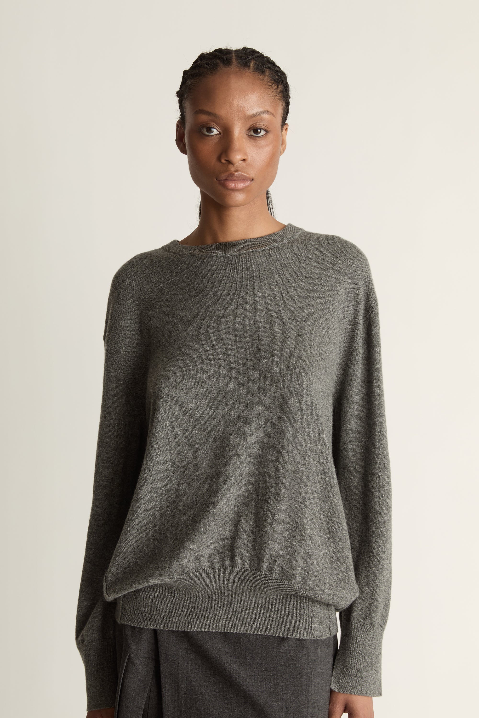Woman wearing a gray sweater and dark gray skirt on a white background