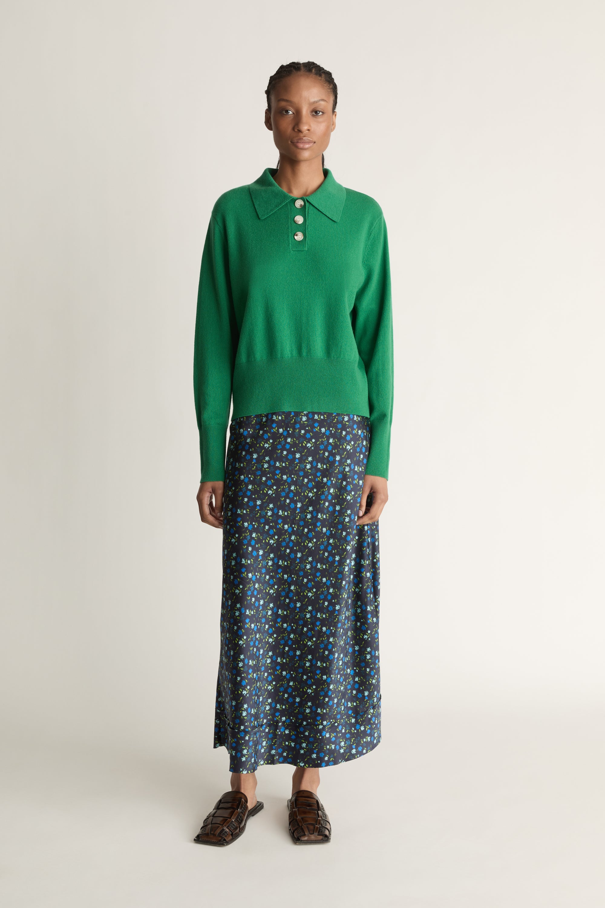 Woman wearing a green sweater and patterned skirt on a white background