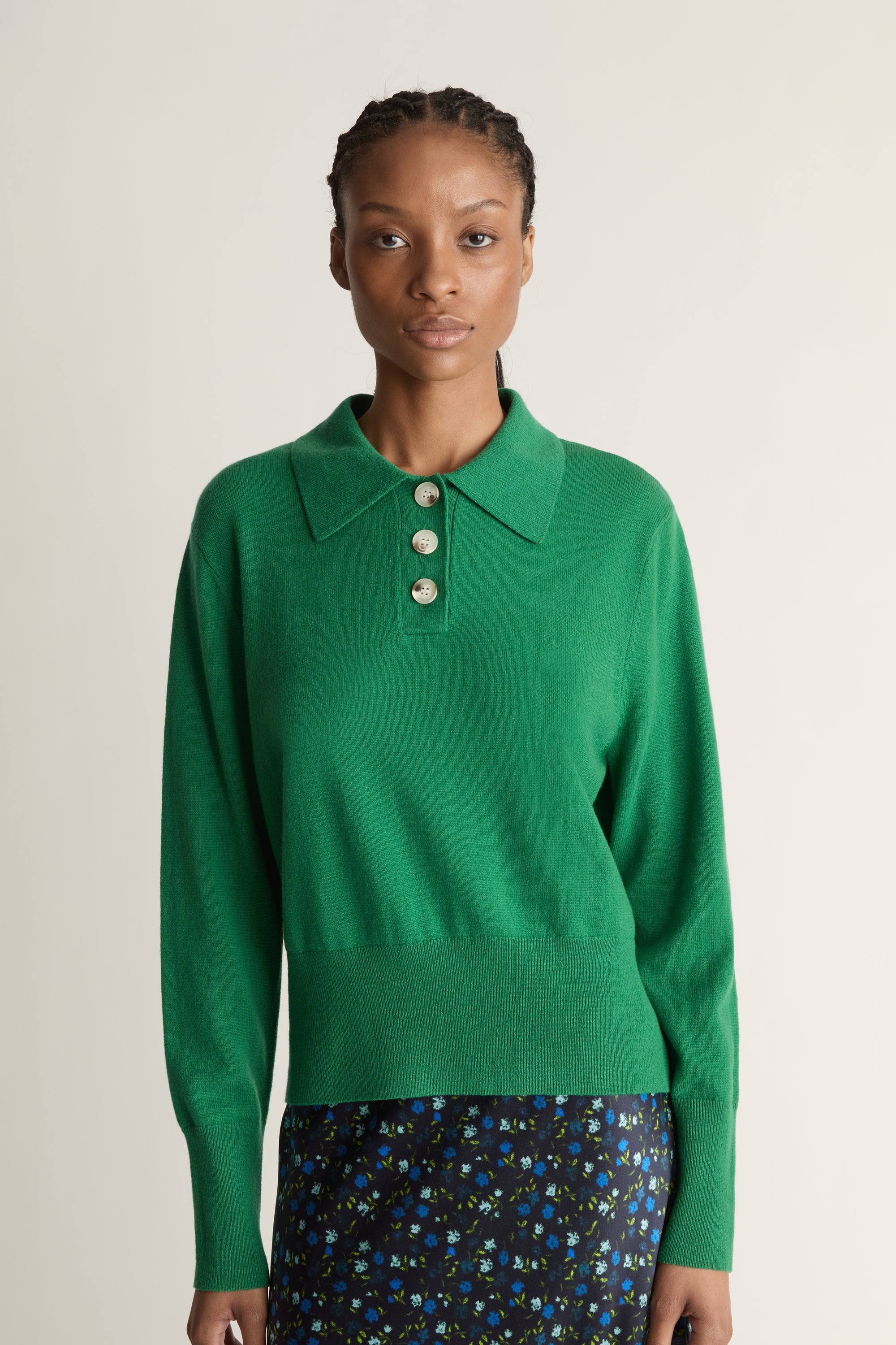 Woman wearing a green sweater and patterned skirt on a white background