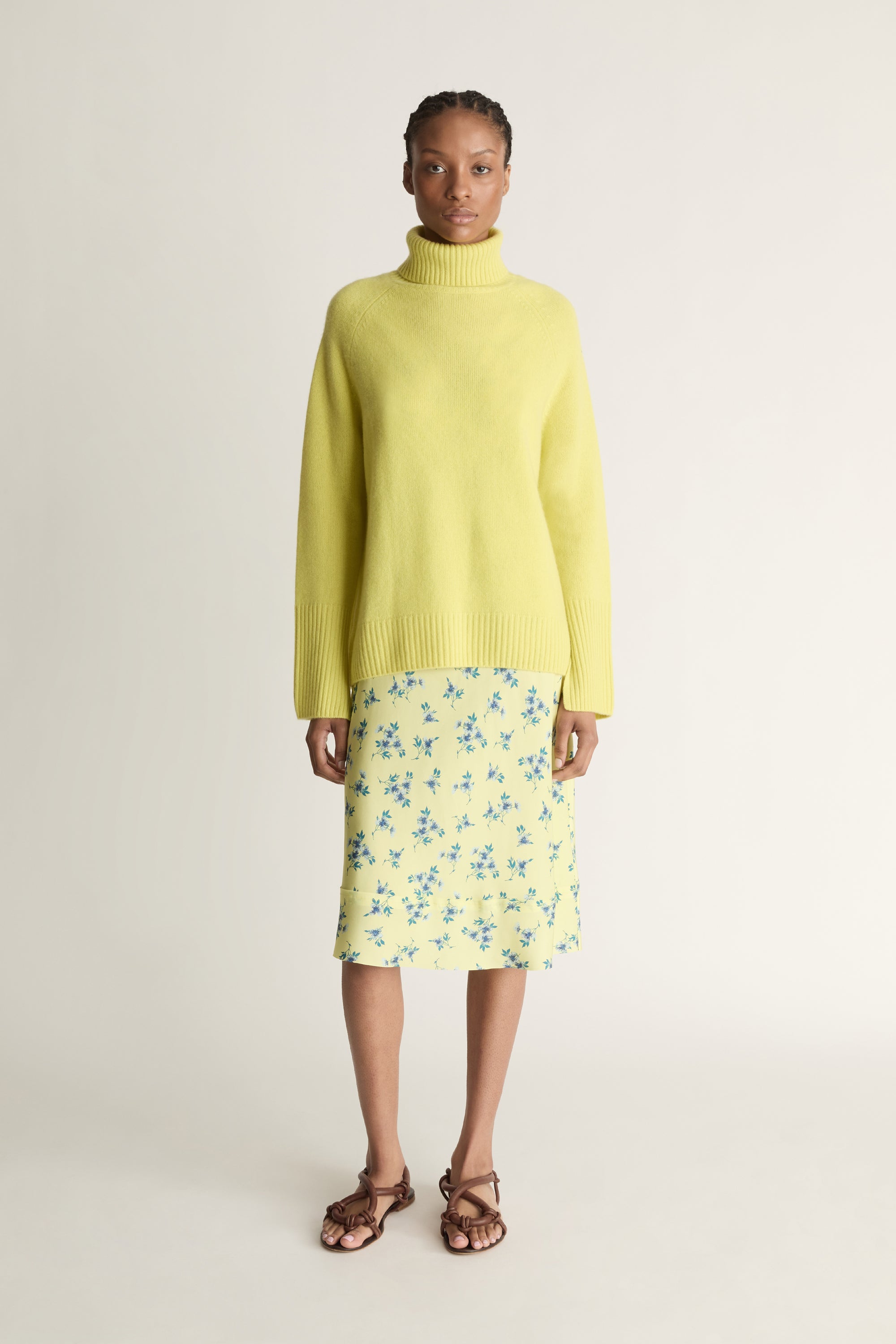 Woman wearing a yellow sweater and floral skirt on a plain background