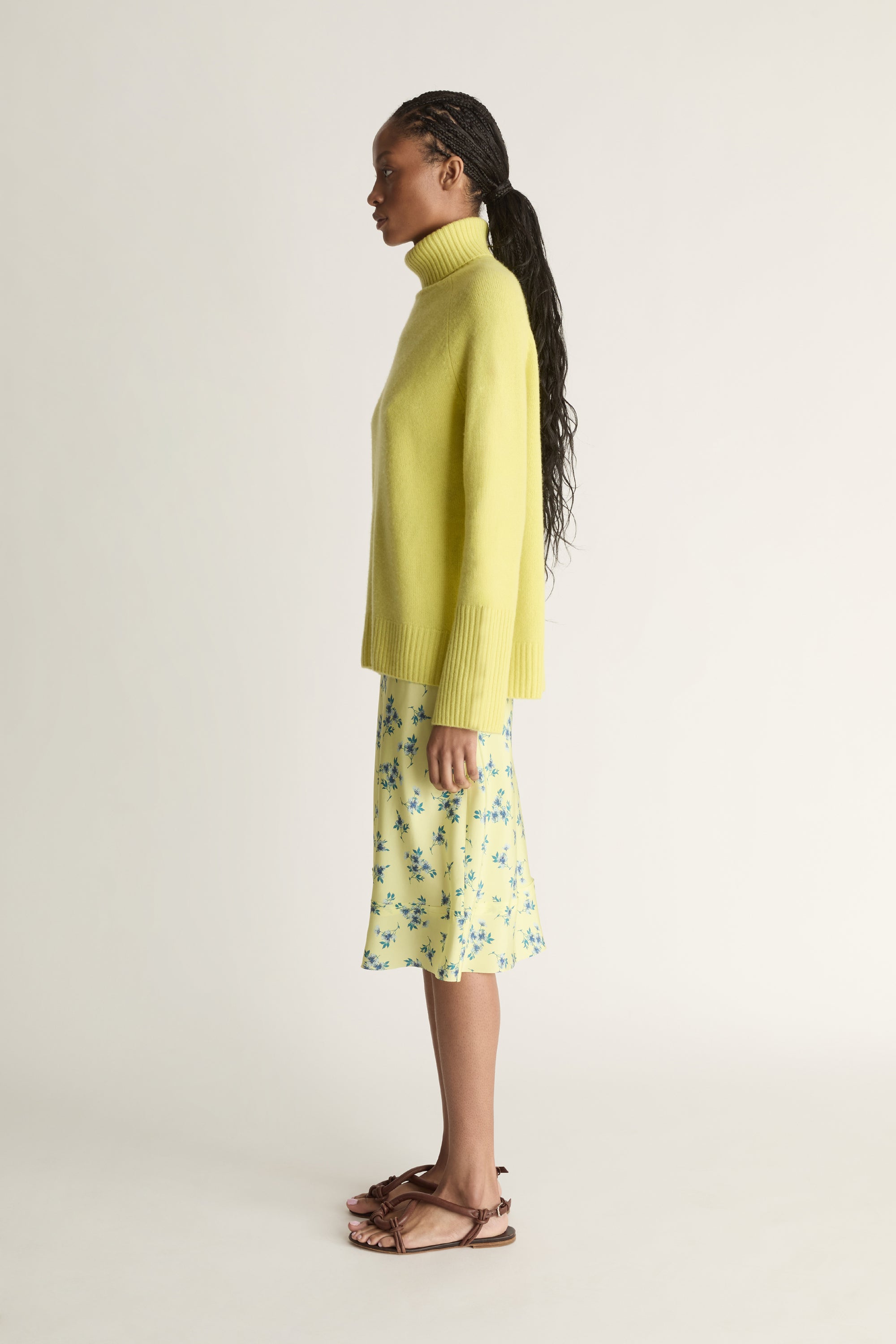 Woman wearing a yellow sweater and floral skirt on a plain background