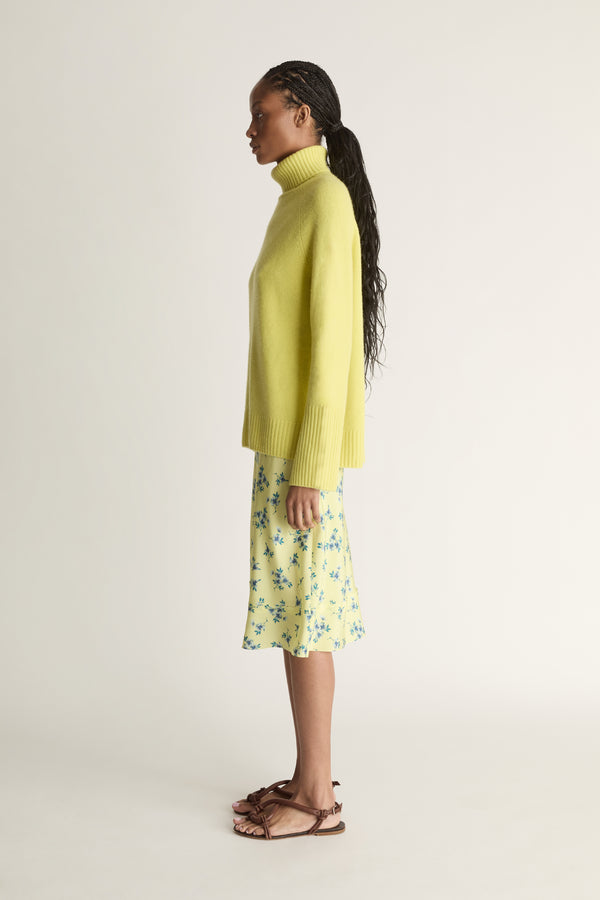 Woman wearing a yellow sweater and floral skirt on a plain background
