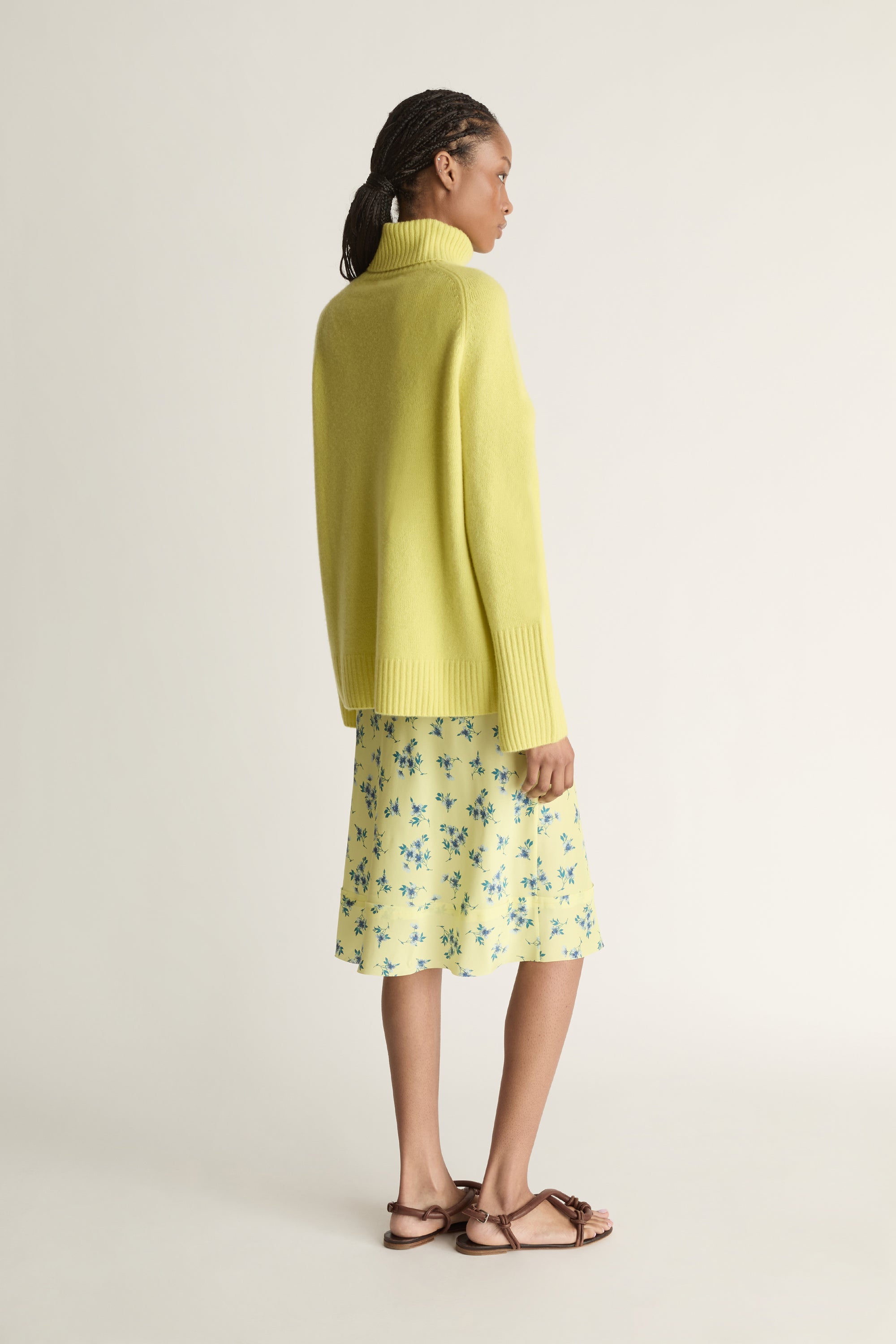 Woman wearing a yellow sweater and floral skirt on a plain background