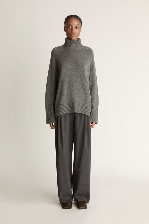 Woman wearing a gray turtleneck sweater and pants on a white background