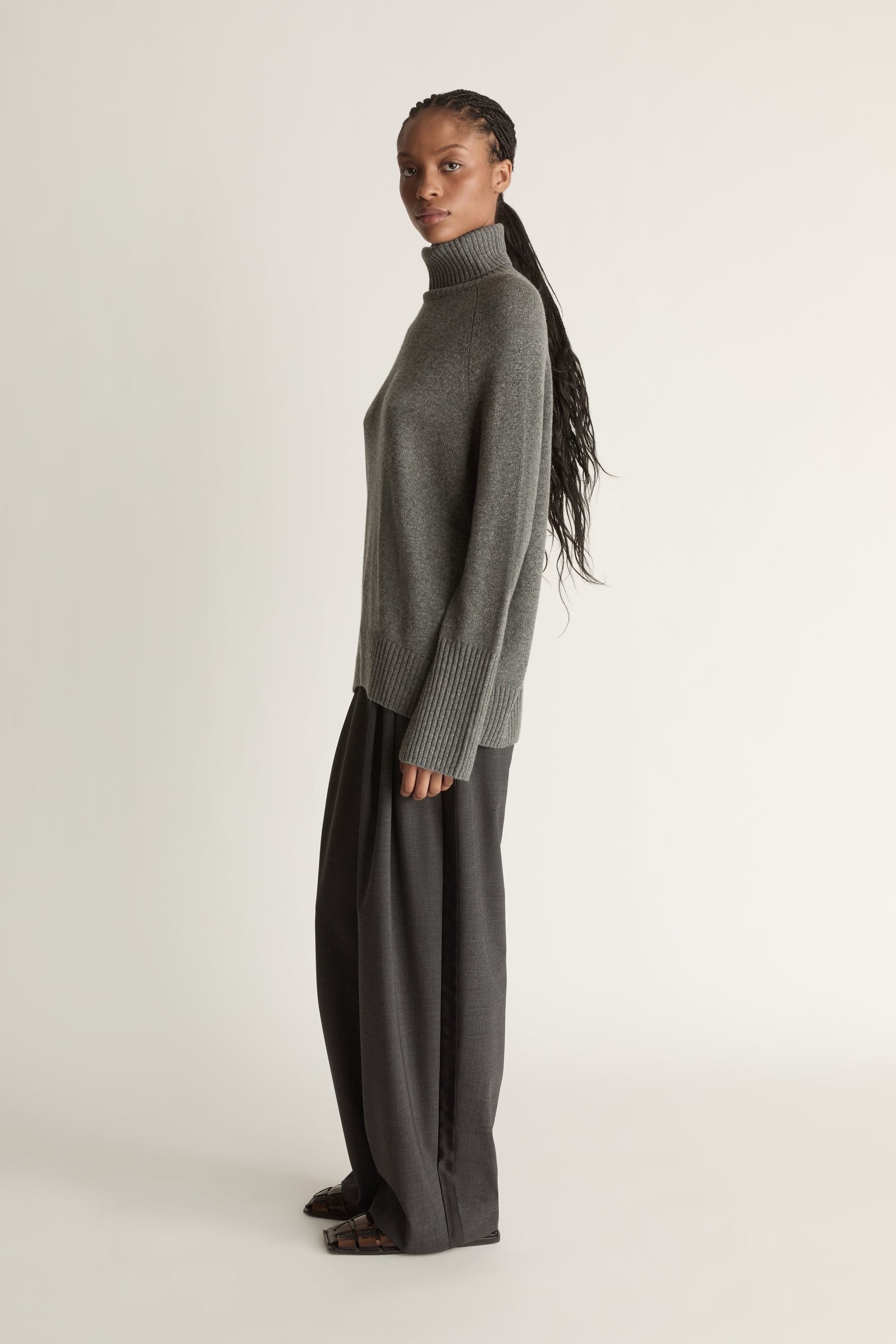 Woman wearing a gray turtleneck sweater and pants on a white background