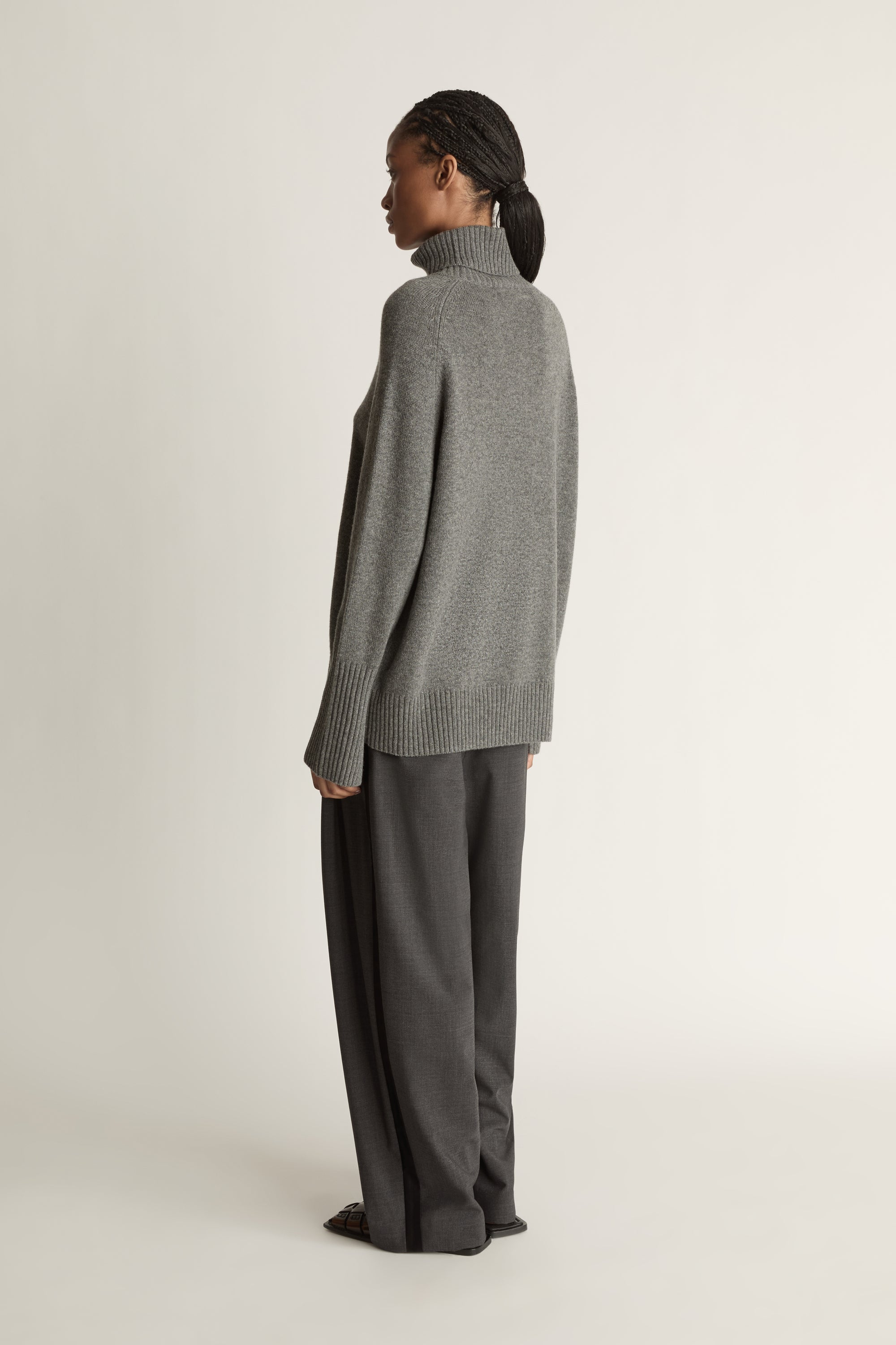 Woman wearing a gray turtleneck sweater and pants on a white background