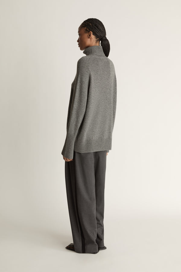 Woman wearing a gray turtleneck sweater and pants on a white background