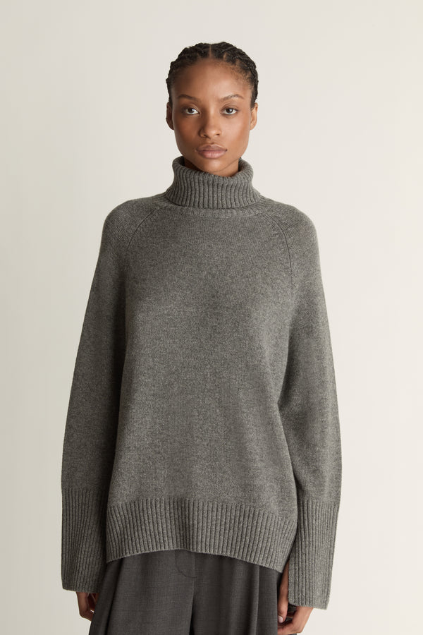 Woman wearing a gray turtleneck sweater and pants on a white background