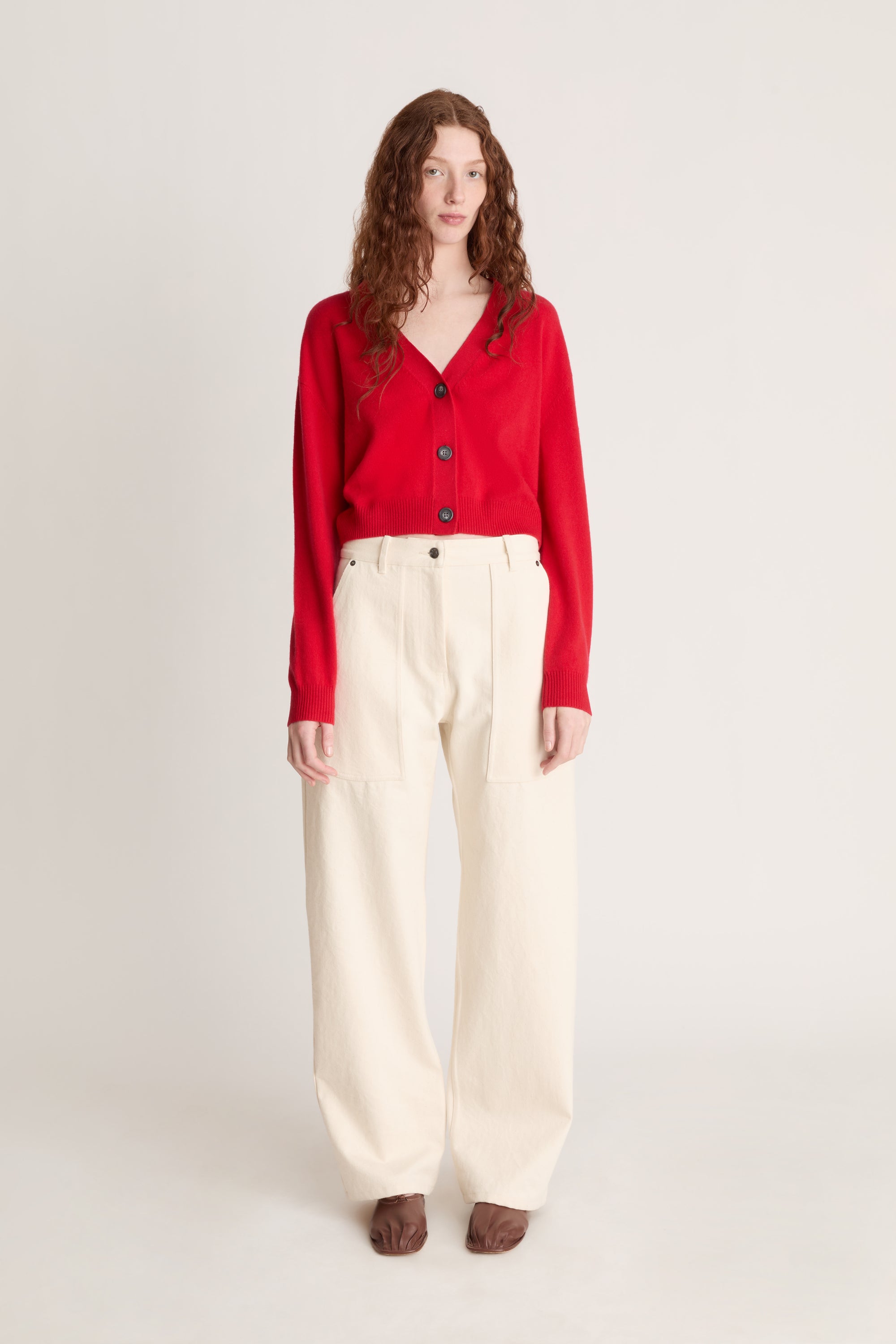 Woman wearing a red cardigan and white pants on a plain background
