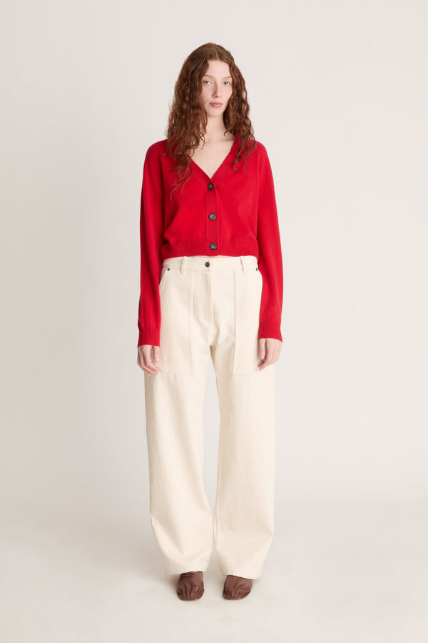 Woman wearing a red cardigan and white pants on a plain background