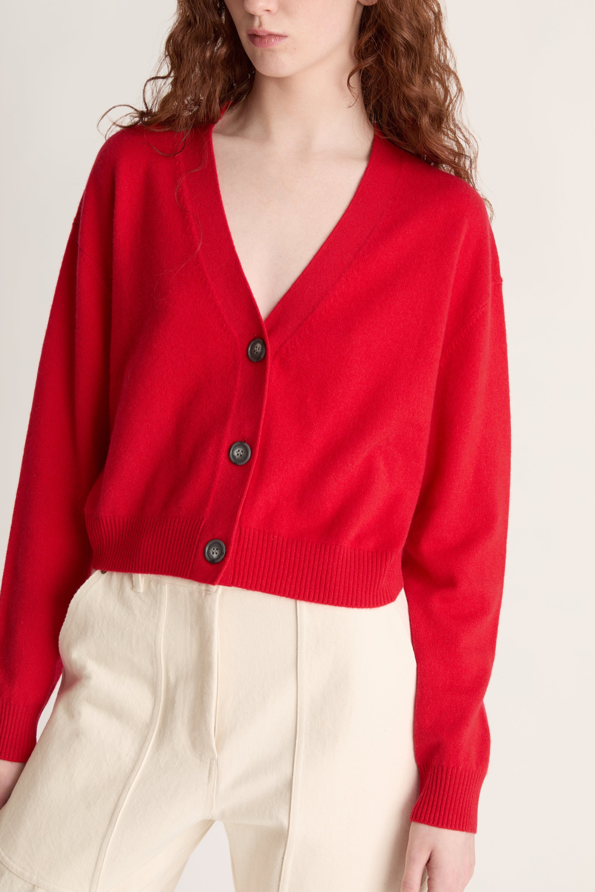 Woman wearing a red cardigan and white pants on a plain background