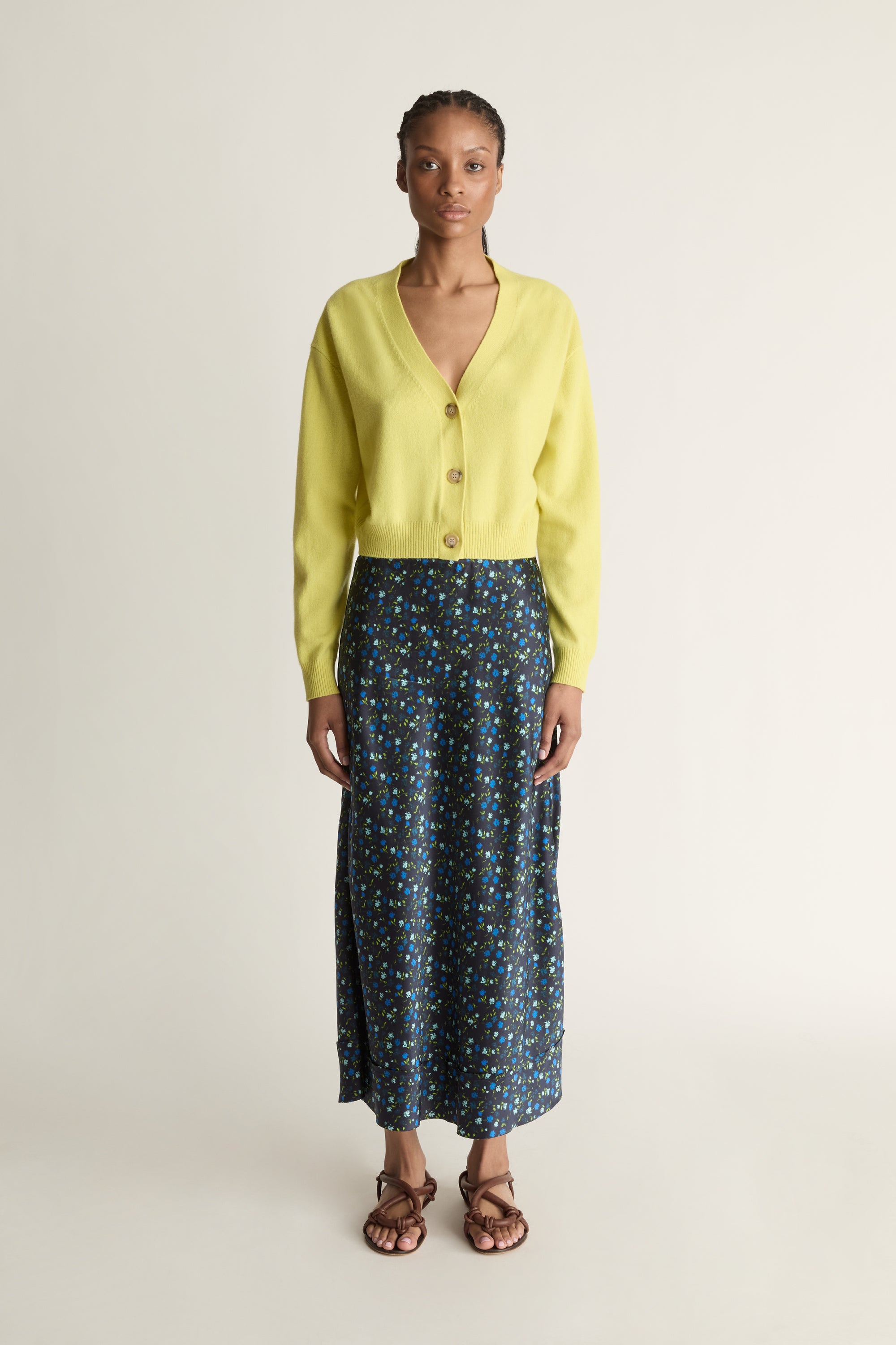Woman wearing a yellow cardigan and patterned skirt on a white background