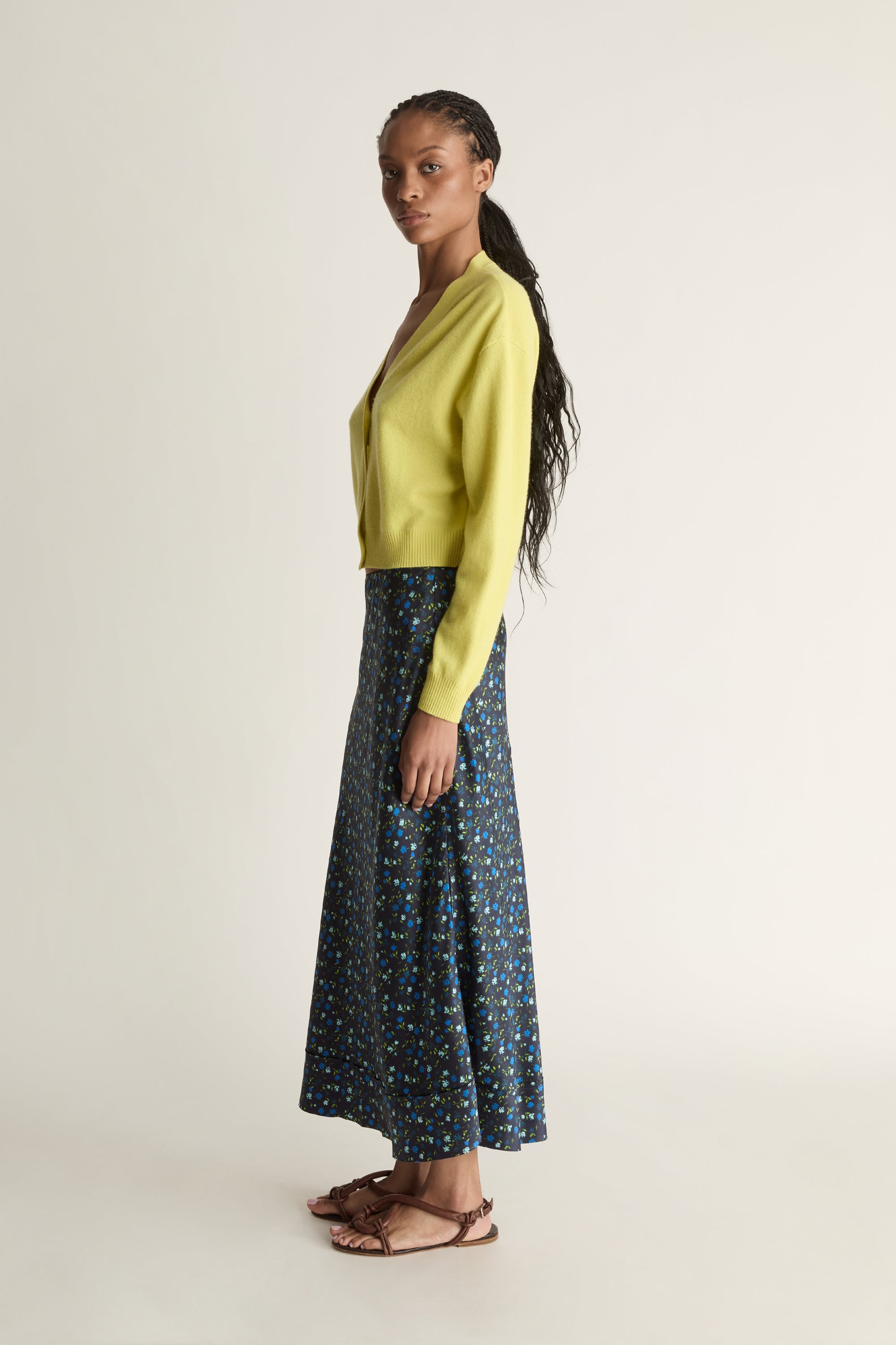 Woman wearing a yellow cardigan and patterned skirt on a white background