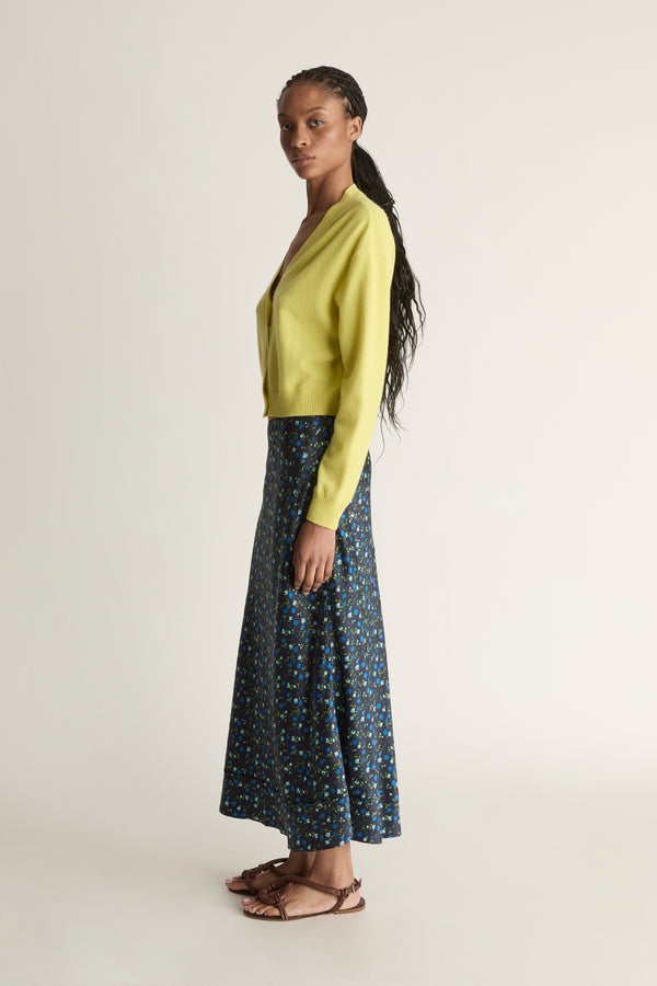 Woman wearing a yellow cardigan and patterned skirt on a white background