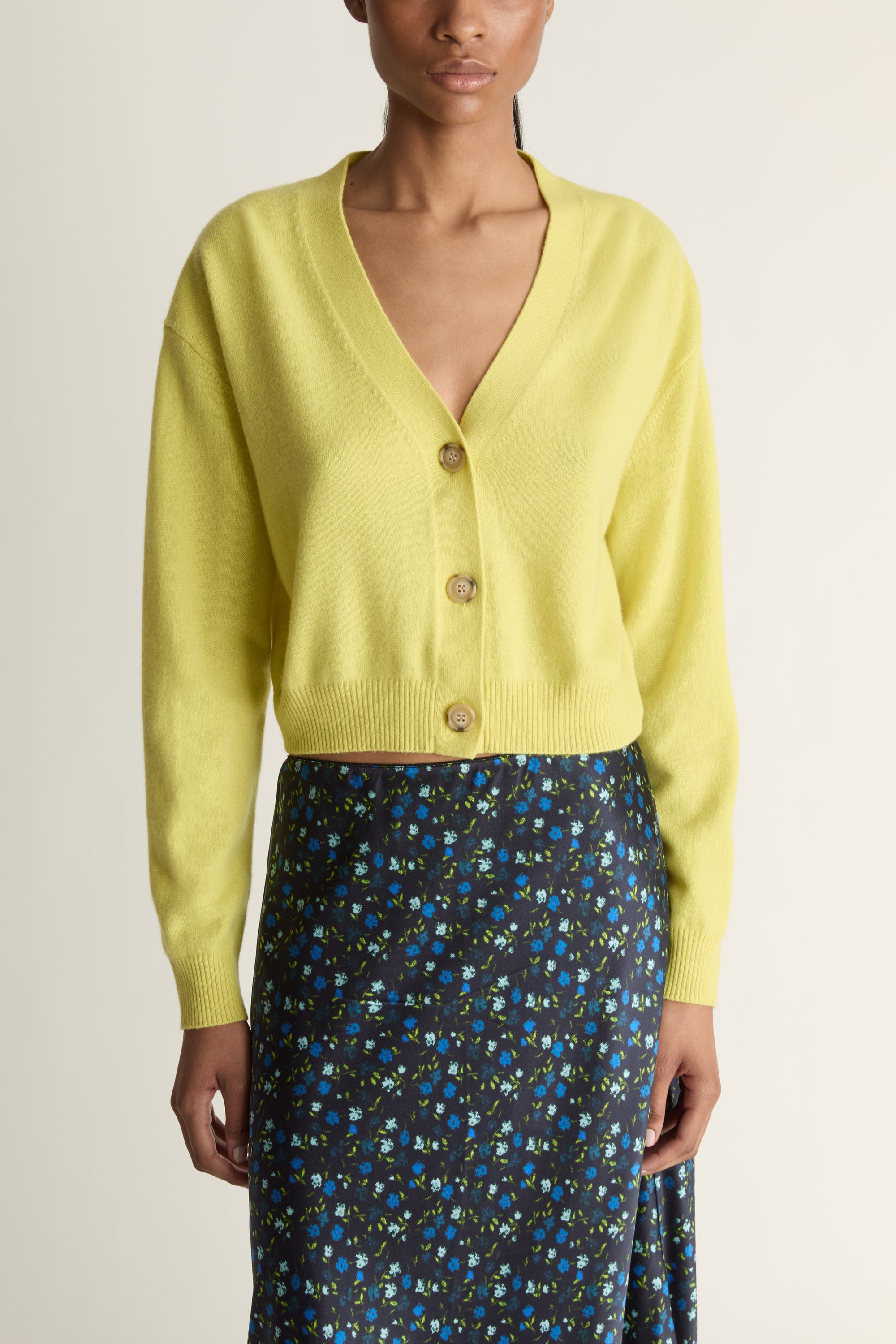 Woman wearing a yellow cardigan and patterned skirt on a white background
