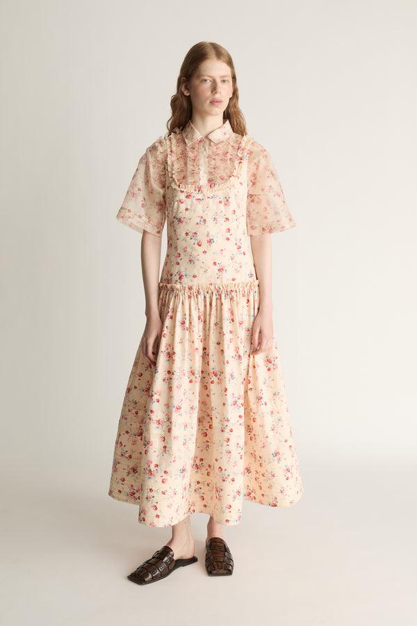 Woman wearing a floral dress  over a floral sheer shirt on a plain background