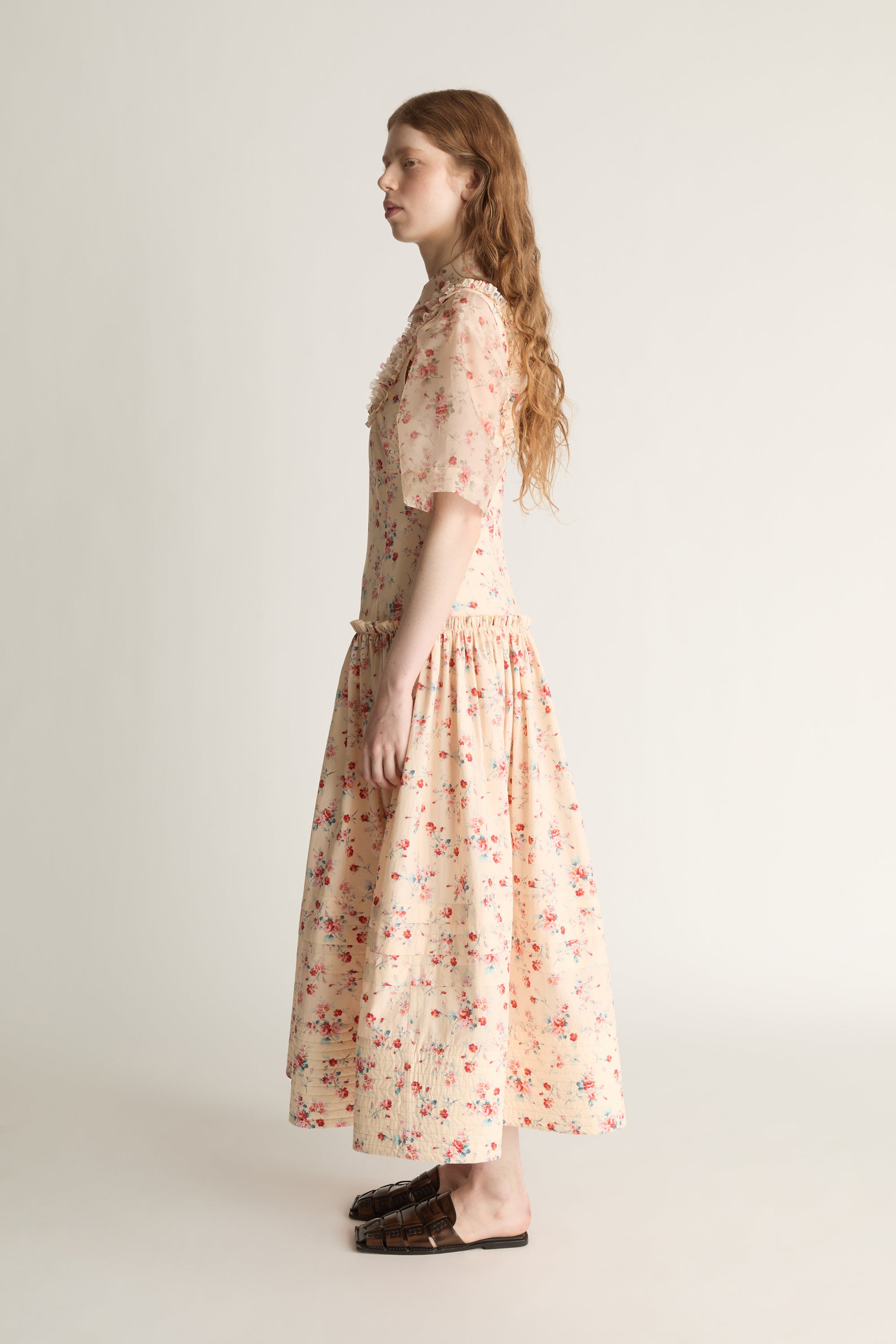 Woman wearing a floral dress  over a floral sheer shirt on a plain background
