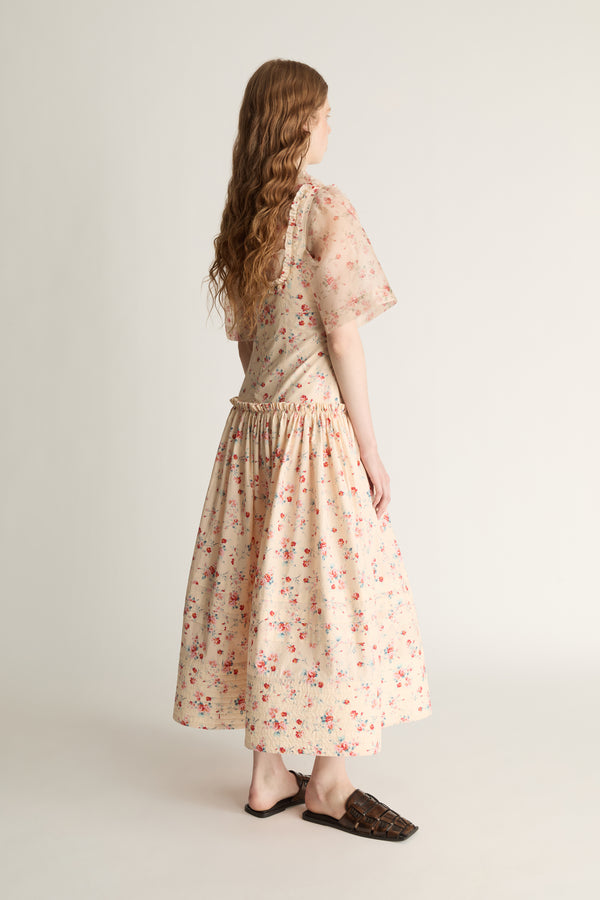Woman wearing a floral dress  over a floral sheer shirt on a plain background