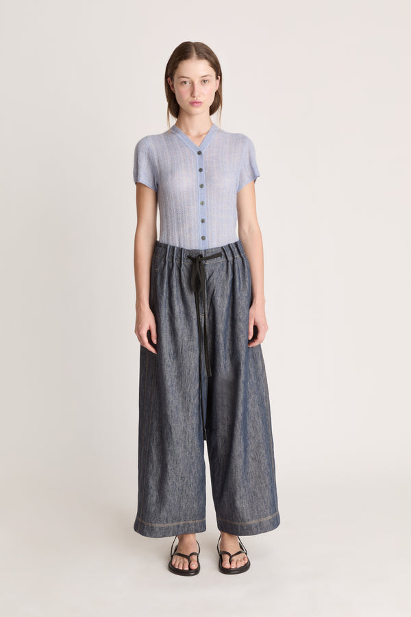 Woman wearing a light blue button-up shirt and dark blue wide-leg pants on a plain background