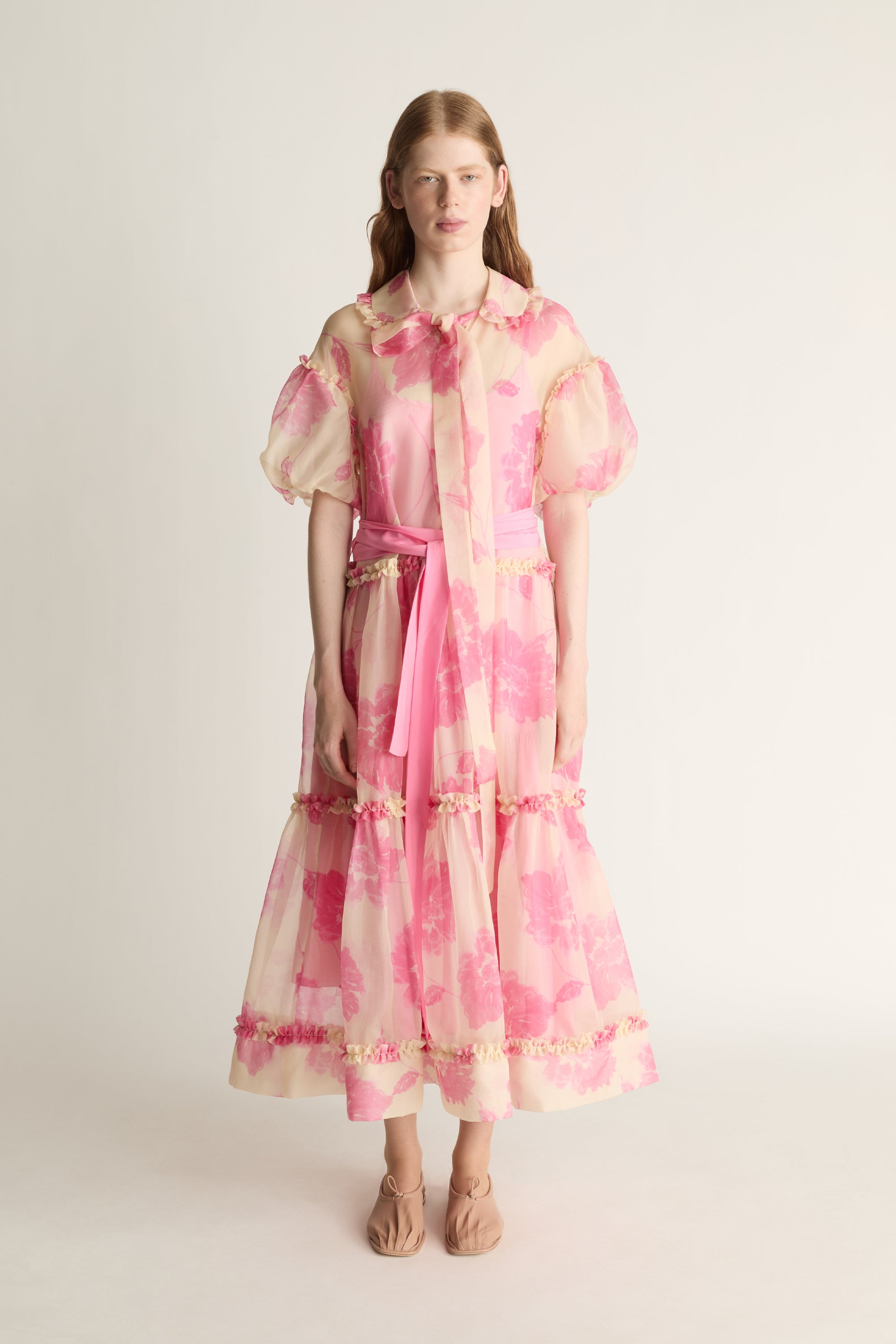 Woman wearing a pink and cream patterned dress on a white background