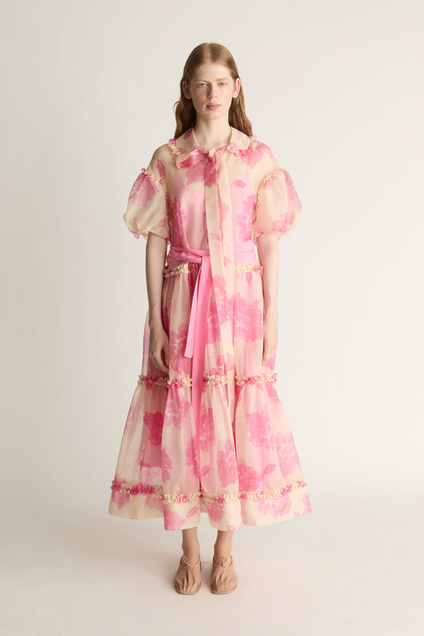 Woman wearing a pink and cream patterned dress on a white background