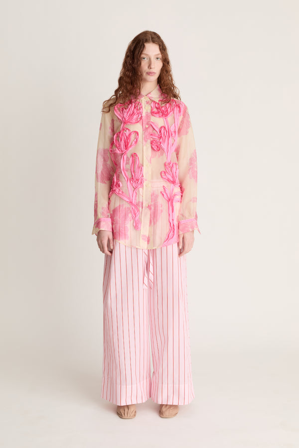Woman wearing a pink floral blouse and striped pants on a white background