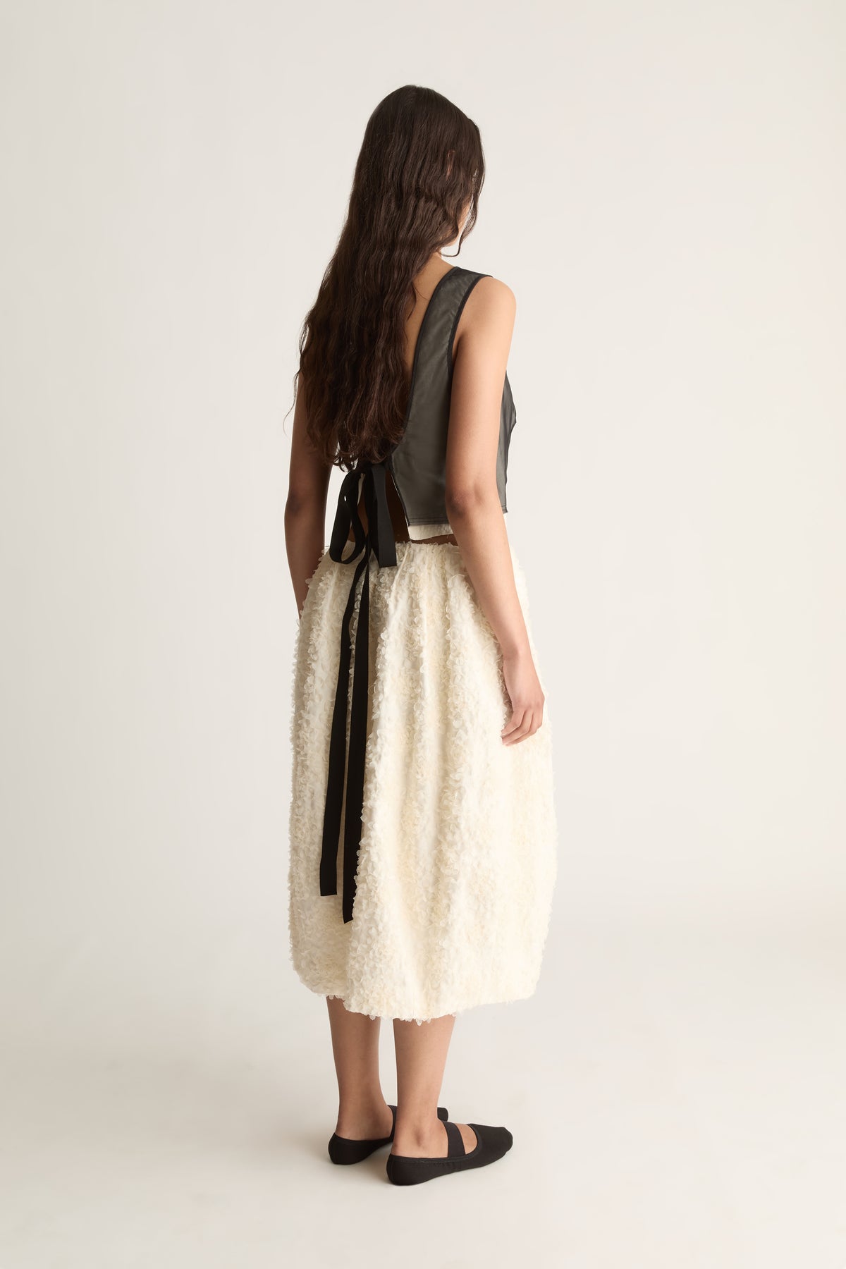 Back view of a cropped sheer black top with an open back tied in a bow with long black ties.