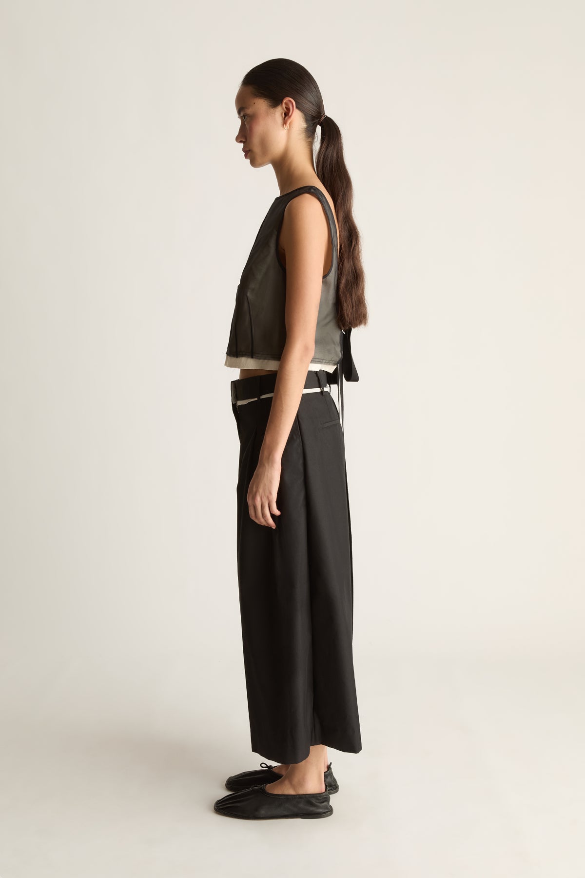 Side view of black wide-leg cropped pants with a pleated front and a hem ending above the ankle.