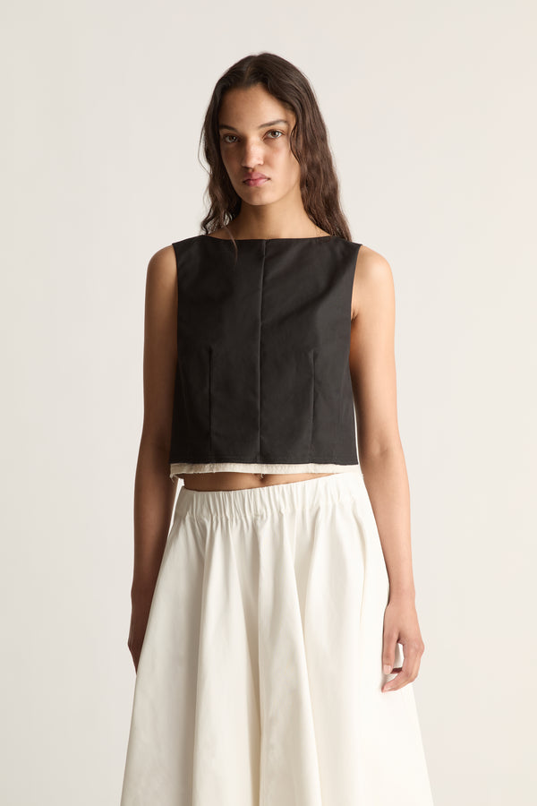 Close-up front view of a cropped sleeveless black top with a round neckline, front seams and cream inner hem.