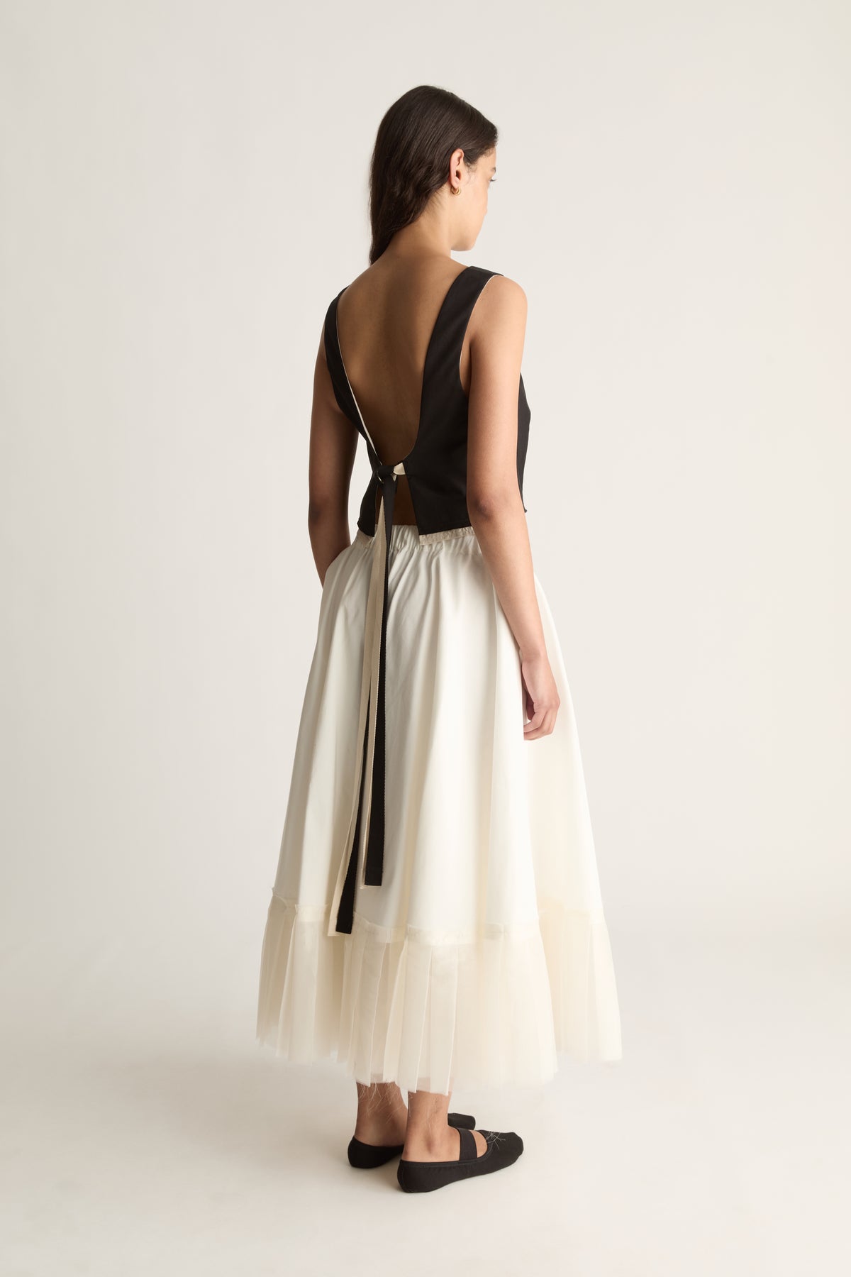 Back view of a cropped black top with a deep open back and long black ties hanging from the waist.