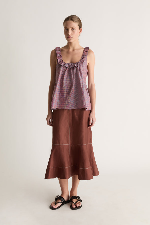 Front view of a woman with hair pulled back in a plum check cami top, brown topstitched midi skirt and black sandals