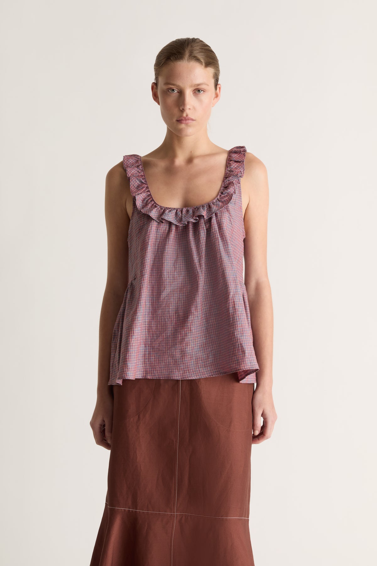 Close-up of a plum check sleeveless top with ruffled scoop neckline and relaxed flared fit, worn with a brown skirt
