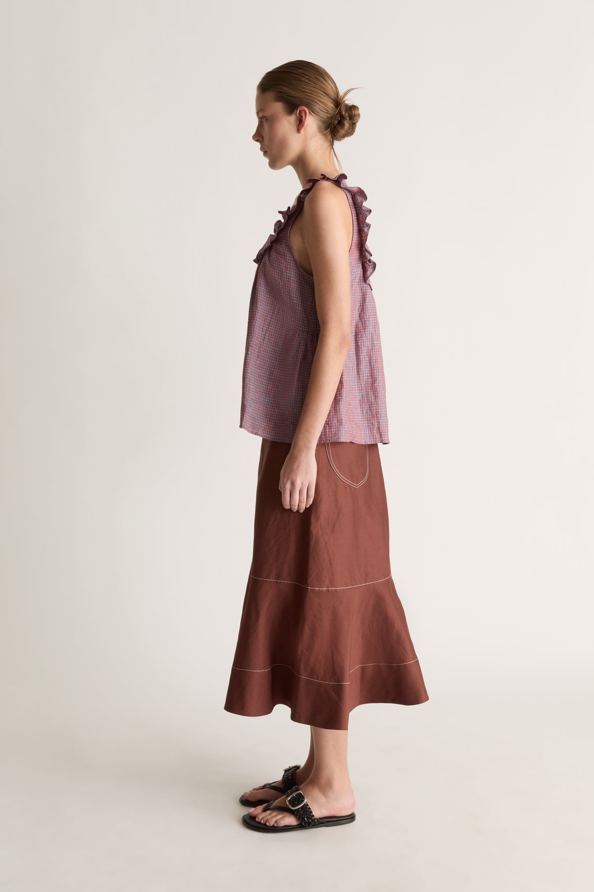 Side profile of a woman with a bun in a plum check ruffle-strap cami top and brown flared midi skirt