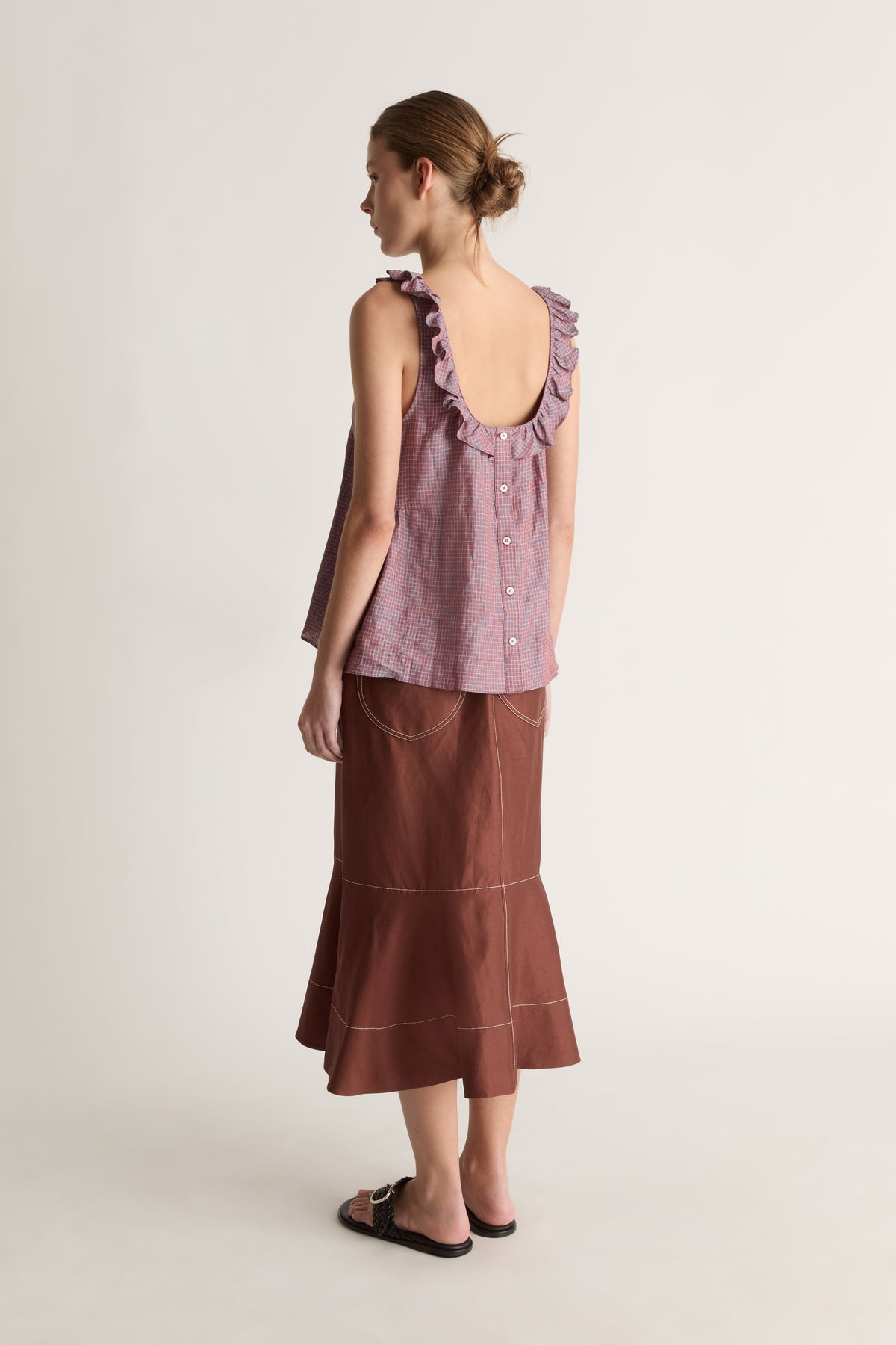 Back view of a woman with a bun in a plum check cami top with scoop back and button closure, and a brown skirt