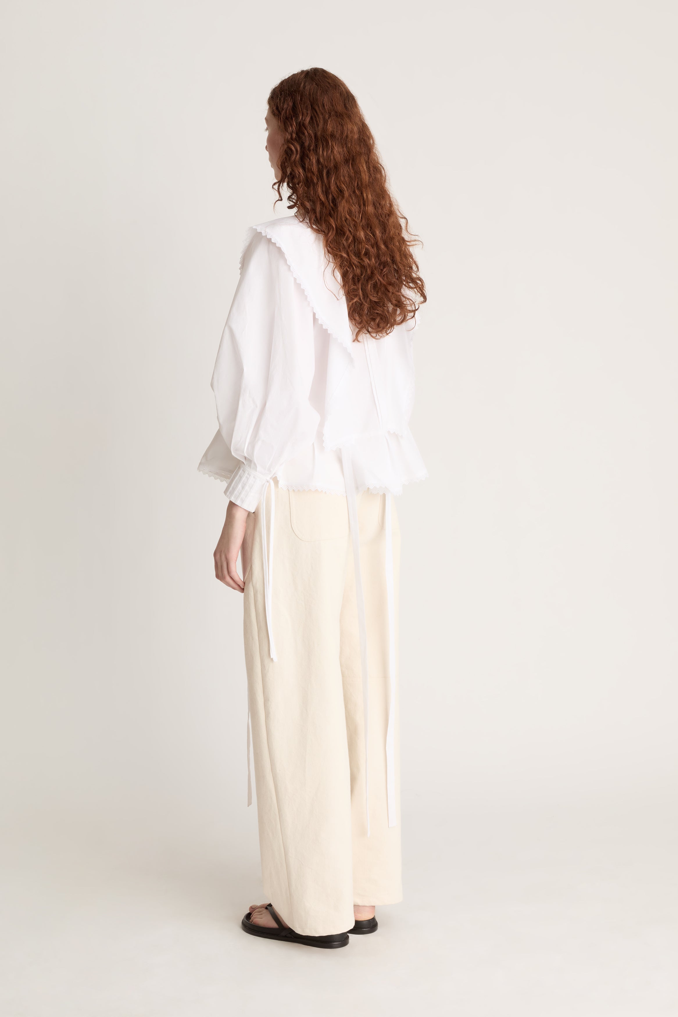 Woman wearing a white blouse and beige pants on a plain background