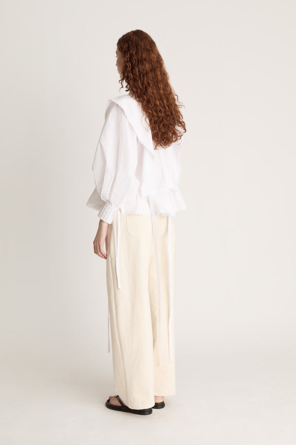 Woman wearing a white blouse and beige pants on a plain background