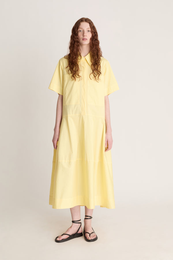 Woman wearing a yellow shirt dress against a plain background